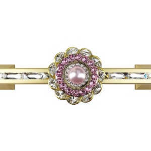 Op de afbeelding: Gouden ladegreep met een roze en helder kristallen bloemontwerp. Het midden van de bloem heeft een parel.