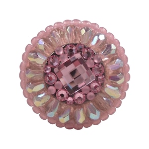 May include: A circular decorative button featuring a central square pink crystal surrounded by smaller round pink rhinestones. The outer edge is adorned with a ring of iridescent, light-reflecting teardrop-shaped beads and a border of small pink beads.