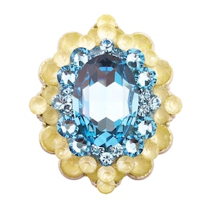 Puede incluir: Una joya con una piedra preciosa ovalada azul claro en el centro, rodeada de piedras preciosas más pequeñas, azul claro y amarillas. El diseño está sobre un fondo blanco, creando un contraste llamativo. La disposición es floral o en forma de estrella.