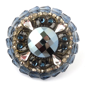 Könnte beinhalten: Eine runde, blaue und silberne Brosche mit einem großen, facettierten, blauen Kristall in der Mitte.