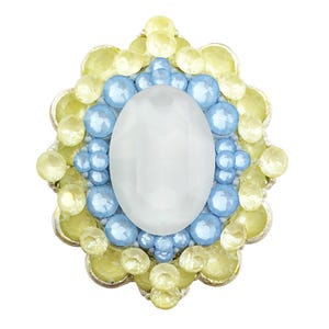 May include: A decorative brooch with a central, oval, faceted, white gemstone. The brooch is surrounded by light blue and yellow-green gemstones, set in a silver-colored metal frame. The design is symmetrical and ornate.