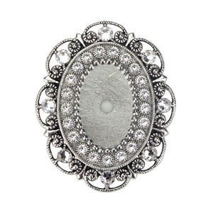 May include: Silver oval-shaped brooch with a decorative filigree design and a clear crystal centre.