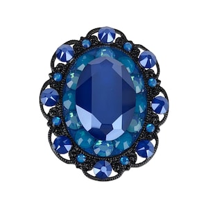 Pode incluir: Broche ovalada azul escuro com uma grande gema central facetada, rodeada por pedras azuis menores e uma moldura preta com filigrana. Design de estilo vintage ou antigo.