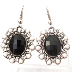Peut inclure: Une paire de boucles d'oreilles pendantes argentées avec une pierre précieuse ovale noire entourée de strass blancs.