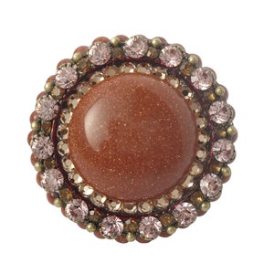 May include: A round, brown, gemstone button with a decorative border of pink and gold rhinestones.