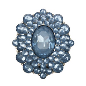 May include: A silver brooch with a large, oval-shaped, light blue rhinestone surrounded by smaller, light blue rhinestones.