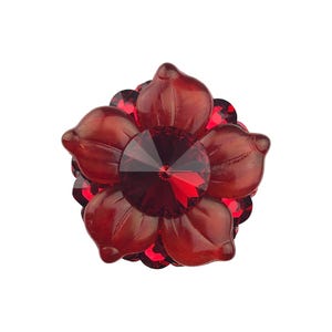 May include: A deep red flower-shaped brooch or decorative pin featuring a central faceted crystal surrounded by layered, translucent red petals. The design displays a symmetrical arrangement with a polished finish and a vibrant, dark crimson color palette.