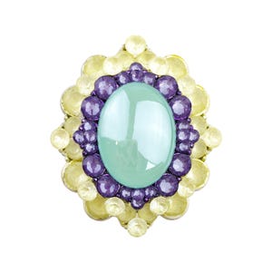May include: An elaborate brooch featuring a large, pale green oval centre stone. This is framed by a ring of purple gems, and then a border of yellow gems. The design is symmetrical and visually striking, with a high level of detail.