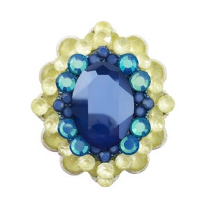 Puede incluir: Broche decorativo con una gran gema azul ovalada en el centro, rodeada de piedras azules y turquesas más pequeñas. El borde exterior está adornado con cristales redondos de color amarillo pálido, creando un diseño floral.