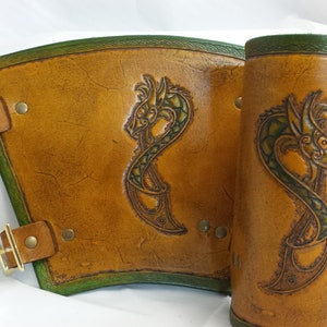 May include: A pair of brown leather arm guards with green dragon designs and brass buckles.