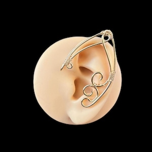 May include: Gold ear cuff with a delicate, intricate design. The cuff is made of wire and has a curved shape that fits around the ear. It is a stylish and unique piece of jewelry.