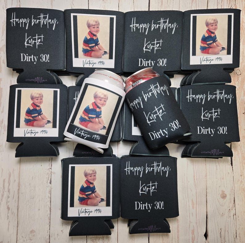 Peut inclure: Plusieurs manchons isothermes noirs pour canettes avec l'inscription blanche "Happy birthday, Kurt! Dirty 30!". Chaque manchon pr&eacute;sente une photo vintage d'un jeune gar&ccedil;on. Une canette est ins&eacute;r&eacute;e dans l'un des manchons. Photo : "Vintage 1994".