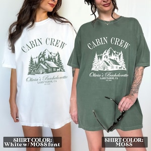 May include: Two oversized t-shirts with the text "Cabin Crew" and "Olivia's Bachelorette Lake Tahoe, CA Est. 2023". The shirt on the left is white with green text and the shirt on the right is green with white text.