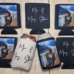 May include: Navy blue can coolers with a photo of a couple and the text "Mr. & Mrs. Stone." Some coolers are shaped like computer monitors. One cooler is white with black text. The photo shows a couple on a deck with a mountain and water background.