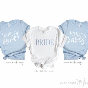 May include: Three crew neck t-shirts. Two are light blue, one is white. The light blue shirts have the text "BABE OF honor" and "BRIDE'S babes" in white script. The white shirt has the word "BRIDE" in light blue block letters.