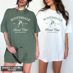 May include: Two oversized t-shirts with the text "Scottsdale Social Club" and "Est. 2024" printed on the front. The shirt on the left is moss green and the shirt on the right is white.