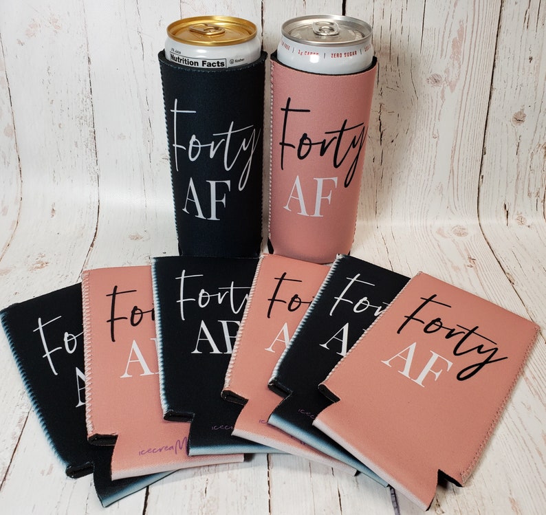 Puede incluir: Un conjunto de ocho enfriadores de latas negros y rosados con el texto "Forty AF" impreso en ellos. Los enfriadores est&aacute;n dispuestos en semic&iacute;rculo sobre una superficie de madera.