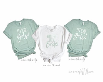 May include: Three t-shirts with different text designs. The first and third shirts are light blue with white text that says "Let's go girls!" The middle shirt is white with light blue text that says "Mani I feel like a Bride!"