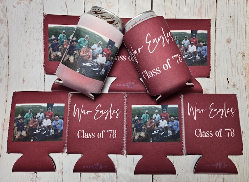 May include: Maroon can coolers with a photo of a group of people and the text "War Eagles Class of '78". One cooler is pink with a photo. The coolers are stacked on a wooden surface.