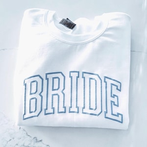 May include: White sweatshirt with the word "BRIDE" in blue outlined letters.