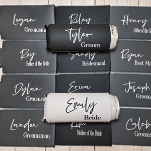 May include: Twelve black and white can coolers with names and titles printed on them. The names include Logan, Riley, Tyler, Sandy, Henry, Ryan, Dylan, Erica, Emily, Joseph, Landon, and Caleb.