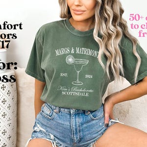 May include: A green t-shirt with the text "MARGS & MATRIMONY" and a margarita glass graphic. The text "EST. 2024" and "Kim's Bachelorette SCOTTSDALE" are also printed on the shirt.