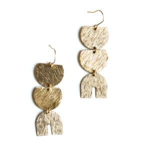 May include: Gold tone geometric earrings with three shapes: two half circles and one arch. The earrings have a brushed finish.