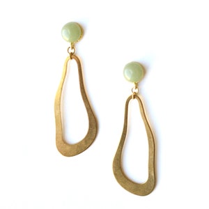 May include: A pair of gold earrings with a green stone accent. The earrings are shaped like an abstract oval with a smooth, curved design.