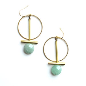 May include: A pair of gold hoop earrings with a geometric design. Each earring features a round hoop with a vertical bar and a horizontal bar, and a light green gemstone pendant.