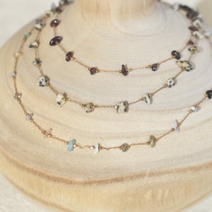 May include: Three layered necklaces with gold chains and various colored stones. The top layer has small, dark purple stones, the middle layer has small, speckled white and black stones, and the bottom layer has small, turquoise stones.
