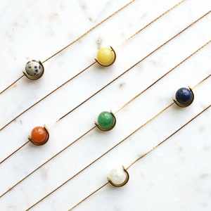 May include: Six gold necklaces with different colored gemstone pendants. The pendants are all in a crescent moon shape. The gemstones are white, green, orange, yellow, blue, and brown.