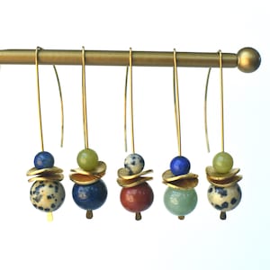 May include: Five pairs of dangle earrings with gold hooks and layered gold discs. Each pair features a different combination of colorful gemstone beads, including green, blue, red, and brown.