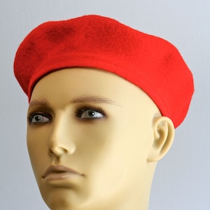 May include: A red beret made of felt. The beret is worn on a mannequin's head.