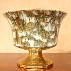 May include: A white ceramic bowl with a green and brown marbled design sits on a gold metal stand. The bowl has a wide, rounded base and a flared lip.