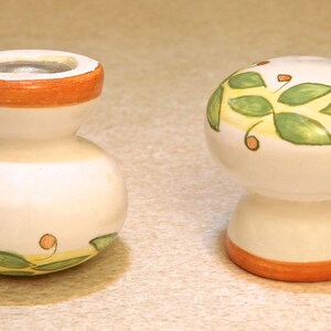 Pu&ograve; includere: Due tappi per bottiglie in ceramica con sfondo bianco e disegni dipinti in verde e arancio. Un tappo ha la forma di un fungo e l'altro &egrave; rotondo con un collo stretto.