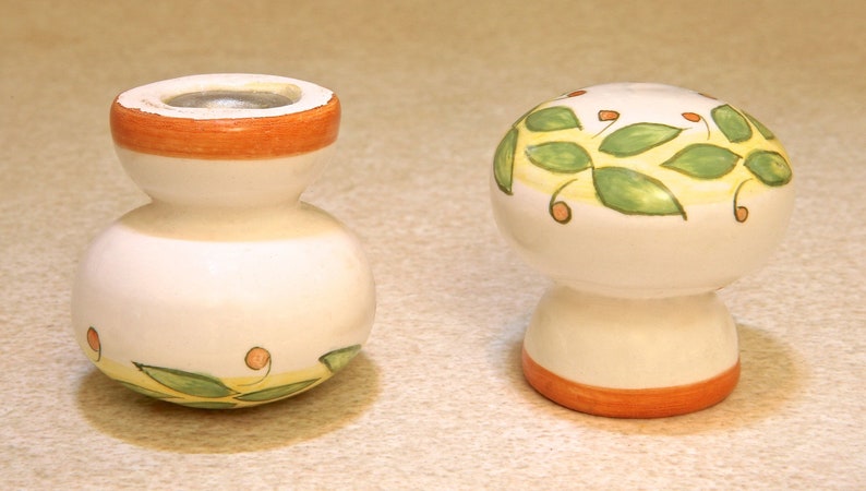 Pu&ograve; includere: Due tappi per bottiglie in ceramica con sfondo bianco e disegni dipinti in verde e arancio. Un tappo ha la forma di un fungo e l'altro &egrave; rotondo con un collo stretto.