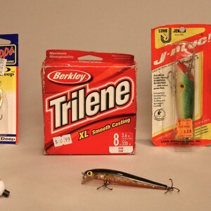 May include: Assortment of fishing lures and tackle, including a red and white bobber, a silver lure, a green and white lure, a black and silver lure, a spool of fishing line, and a package of fishing hooks.