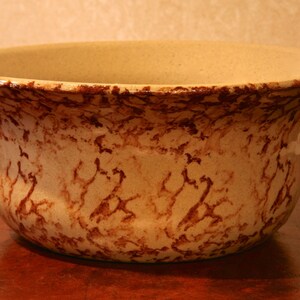 May include: A large, brown and cream ceramic bowl with a mottled glaze. The bowl has a wide, rounded base and a flared rim.