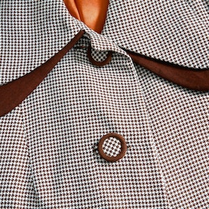 Puede incluir: Una tela de pata de gallo marrón y blanca con un cuello marrón y dos botones marrones.