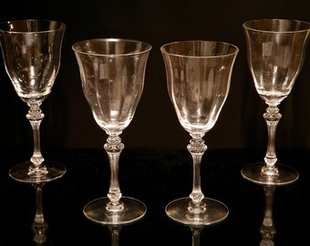 May include: Four clear glass wine glasses with a fluted design. The glasses are arranged in a row on a black surface.