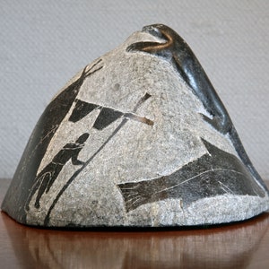 Pode incluir: Uma escultura de pedra cinzenta de uma foca, uma pessoa e um peixe. A escultura é esculpida em um estilo realista e representa a foca escalando uma rocha.