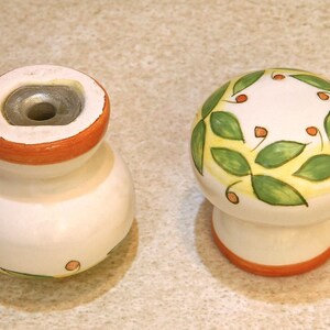 Pu&ograve; includere: Due pomelli in ceramica con base bianca e bordo arancione. Un pomello ha un disegno di foglie verdi e gialle con punti rossi. L'altro pomello ha un foro nella parte superiore.