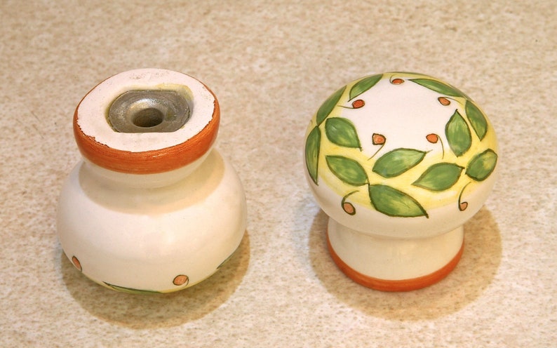 Pu&ograve; includere: Due pomelli in ceramica con base bianca e bordo arancione. Un pomello ha un disegno di foglie verdi e gialle con punti rossi. L'altro pomello ha un foro nella parte superiore.