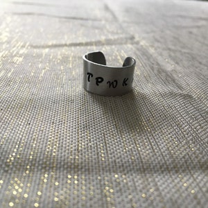 May include: A silver ring with the word "TPWK" engraved on it.