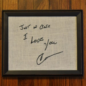 May include: A framed piece of fabric with the handwritten message "Just in case I love you" and a signature.