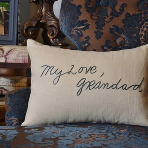 Puede incluir: Una almohada beige con las palabras "My love, Grandad" bordadas en hilo negro.