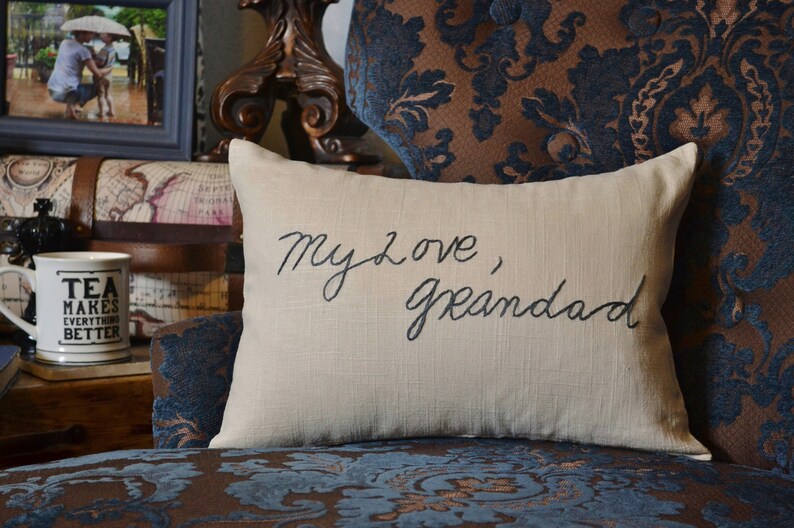 Puede incluir: Una almohada beige con las palabras "My love, Grandad" bordadas en hilo negro.