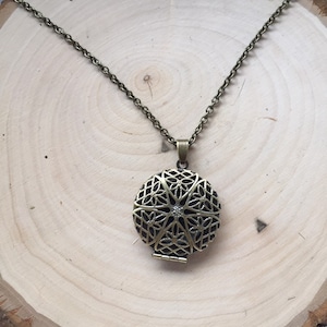 Könnte beinhalten: Eine goldfarbene Halskette mit einem runden, filigranen Anhänger in Form eines Medaillons. Das Medaillon hat ein detailliertes Design mit einem kleinen, klaren Stein in der Mitte.