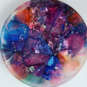 May include: A round, resin art coaster with a swirling pattern of blue, pink, purple, and white. The colors are blended together to create a unique and abstract design.