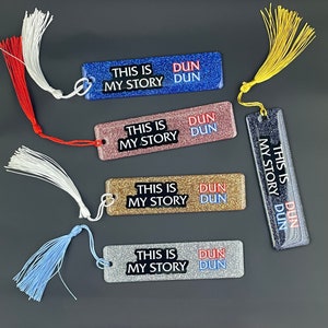 May include: Set of five glittery bookmarks with tassels. Each bookmark features the text "This is my story" and "Dun Dun" in red and blue lettering.